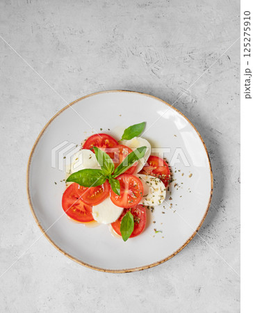 Caprese salad with sliced tomatoes, mozzarella and basil on a plate on a light background 125275910