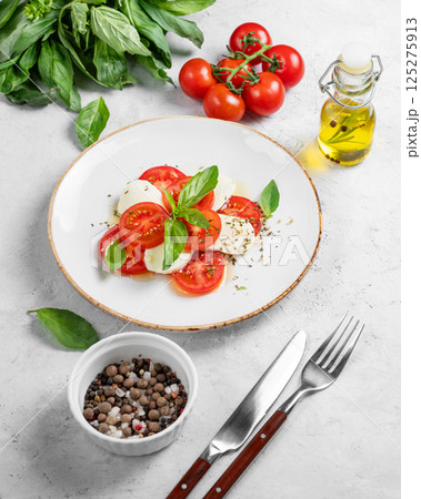 Caprese salad with sliced tomatoes, mozzarella and basil  on a light background 125275913