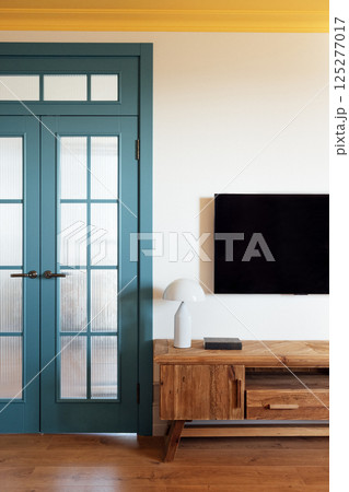 The elements of the stylish modern interior of the living room. Wooden chest of drawers with a lamp. Elegant blue glazed doors. The bright yellow ceiling. 125277017