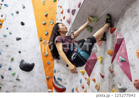 A young Asian woman on a climbing wall. A Korean girl climbs a bouldering wall A young Asian woman on a climbing wall. A Korean girl climbs a bouldering wall 125277043