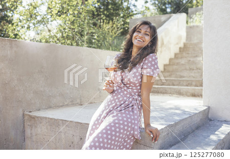 Beautiful young mixed race woman in pink dress smiling and holding glass of champagne 125277080