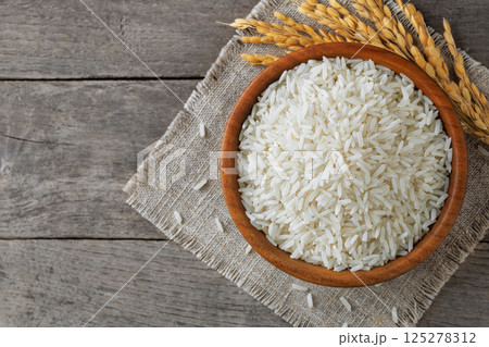 White rice filling wooden bowl on rustic table, complemented by delicate stalks 125278312