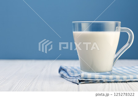 milk in glass cup resting on checkered cloth on white wooden table with blue background milk in glass cup resting on checkered cloth on white wooden table with blue background 125278322