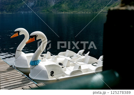 White swanshaped pedal boats moored wooden pier mountain lake. Beautiful scenic landscape mountains background clear blue water leisure recreation activity. 125278389