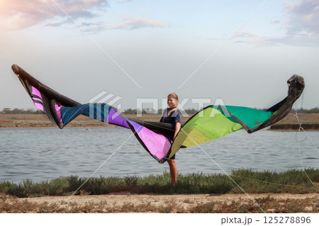 A woman with a multicolored parachute, an athlete riding kitersurfing on a blue pore. Beach, active recreation. Sunset competitions, parachute, board, freedom. High quality photo A woman with a multicolored parachute, an athlete riding kitersurfing on a blue pore. Beach, active recreation. Sunset competitions, parachute, board, freedom. High quality photo 125278896