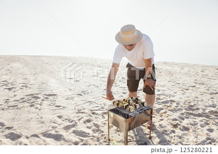 A young man in a summer casual outfit is having a barbecue on beach. A young man in a summer casual outfit is having a barbecue on beach. 125280221