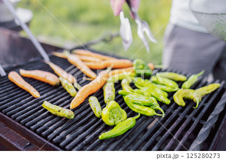 Close-up of a vegetarian barbecue and a cooking man. Tasty fried peppers and carrots on the grill. Vegetables are cooked on coals on the bars in the open air. 125280273