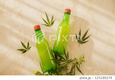 Two plastic juice bottles on a marble table with cannabis leaves. 125280274