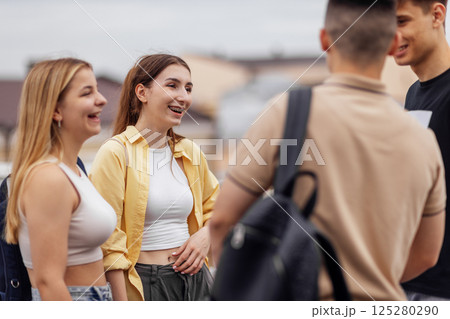 Four teenagers in casual clothes chat and laugh on the roof of the house 125280290