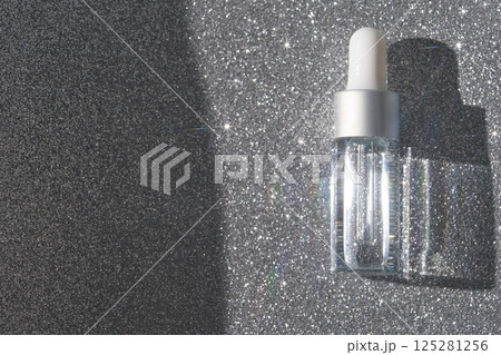 Transparent dropper bottle on glittery silver background with shimmering light Transparent dropper bottle on glittery silver background with shimmering light 125281256