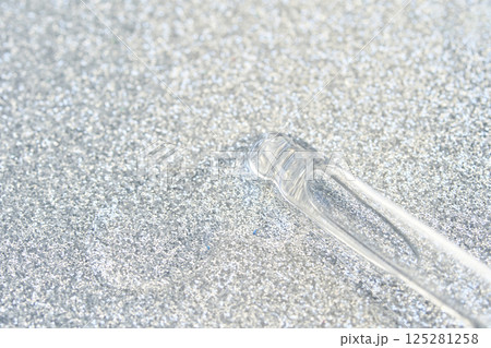 Transparent glass dropper on sparkling silver glitter background texture shine 125281258