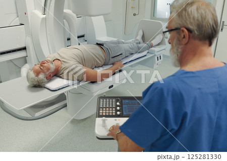 Male patient undergoing X-ray examination using tilting radiographic wall stand. 125281330