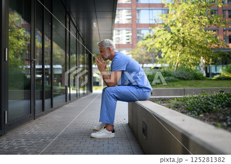 Frustrated and burnt-out doctor standing outside the hospital, feeling down. Frustrated and burnt-out doctor standing outside the hospital, feeling down. 125281382
