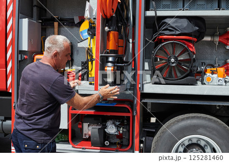 A dedicated firefighter preparing a modern firetruck for deployment to hazardous fire-stricken areas, demonstrating readiness and commitment to emergency response A dedicated firefighter preparing a modern firetruck for deployment to hazardous fire-stricken areas, demonstrating readiness and commitment to emergency response 125281460