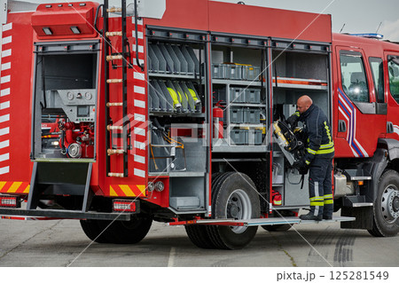A firefighter meticulously prepares a modern firetruck for a mission to evacuate and respond to dangerous situations, showcasing the utmost dedication to safety and readiness in the face of a fire A firefighter meticulously prepares a modern firetruck for a mission to evacuate and respond to dangerous situations, showcasing the utmost dedication to safety and readiness in the face of a fire 125281549