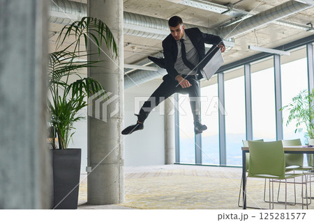 A businessman ecstatically jumping in a modern office, holding a briefcase in his hands, celebrating a moment of success and triumph. 125281577