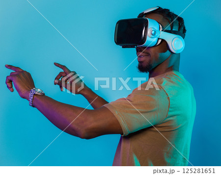 Immersed in a digital realm, an African American man navigates the virtual landscape with a VR goggles, using tactile gestures to interact with virtual objects, showcasing a harmonious blend of 125281651