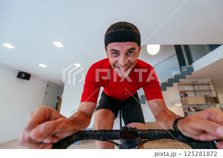 A triathlete riding a triathlon bike on a machine simulation in a modern living room. Training during pandemic conditions. A triathlete riding a triathlon bike on a machine simulation in a modern living room. Training during pandemic conditions. 125281872