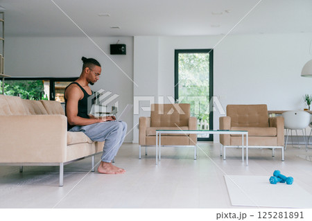 African American man in glasses sitting at a table in a modern living room, using a laptop for business video chat, conversation with friends and entertainment. African American man in glasses sitting at a table in a modern living room, using a laptop for business video chat, conversation with friends and entertainment. 125281891