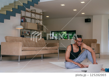 Training At Home. Sporty African American man doing the training while watching an online tutorial on a laptop, exercising in the living room, free space 125282003