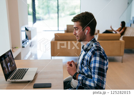 A freelancer sitting at a table in a modern living room, with headphones using a laptop for business video chat, conversation with friends and entertainment A freelancer sitting at a table in a modern living room, with headphones using a laptop for business video chat, conversation with friends and entertainment 125282015