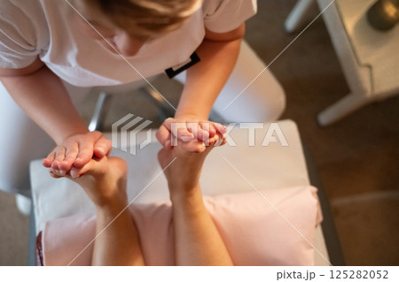 Foot Massage Therapy in a Relaxing Spa Setting. A professional massage therapist in a white uniform provides a soothing foot massage to a client in a calm and serene spa environment Foot Massage Therapy in a Relaxing Spa Setting. A professional massage therapist in a white uniform provides a soothing foot massage to a client in a calm and serene spa environment 125282052