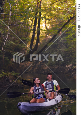 A young couple enjoying an idyllic kayak ride in the middle of a beautiful river surrounded by forest greenery A young couple enjoying an idyllic kayak ride in the middle of a beautiful river surrounded by forest greenery 125282153