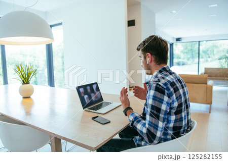 A freelancer sitting at a table in a modern living room, with headphones using a laptop for business video chat, conversation with friends and entertainment 125282155