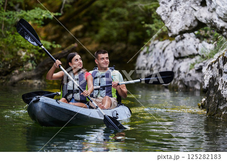 A young couple enjoying an idyllic kayak ride in the middle of a beautiful river surrounded by forest greenery 125282183