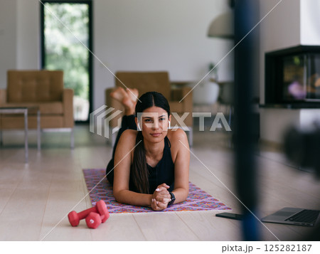 Young woman resting after online training while lying on the living room floor. Young woman resting after online training while lying on the living room floor. 125282187