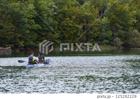 A young couple enjoying an idyllic kayak ride in the middle of a beautiful river surrounded by forest greenery 125282229