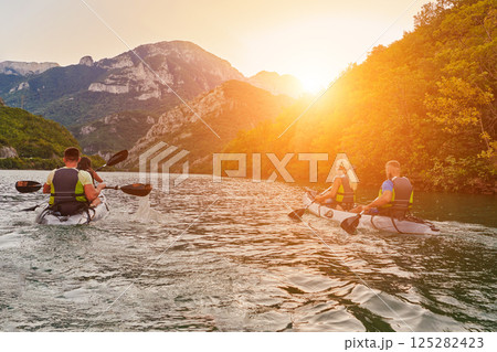 A group of friends enjoying fun and kayaking exploring the calm river, surrounding forest and large natural river canyons during an idyllic sunset. 125282423