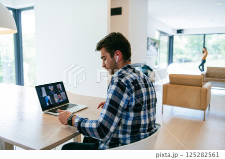 A freelancer sitting at a table in a modern living room, with headphones using a laptop for business video chat, conversation with friends and entertainment 125282561