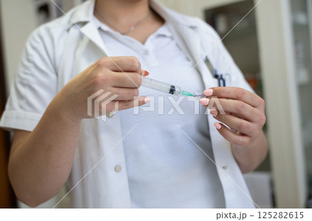 A focused nurse in a white lab coat carefully prepares a syringe for an injection in a professional healthcare environment. A focused nurse in a white lab coat carefully prepares a syringe for an injection in a professional healthcare environment. 125282615