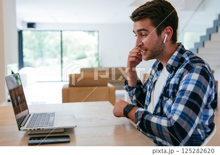 A freelancer sitting at a table in a modern living room, with headphones using a laptop for business video chat, conversation with friends and entertainment A freelancer sitting at a table in a modern living room, with headphones using a laptop for business video chat, conversation with friends and entertainment 125282620