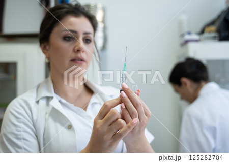 A focused nurse in a white lab coat carefully prepares a syringe for an injection in a professional healthcare environment. A focused nurse in a white lab coat carefully prepares a syringe for an injection in a professional healthcare environment. 125282704