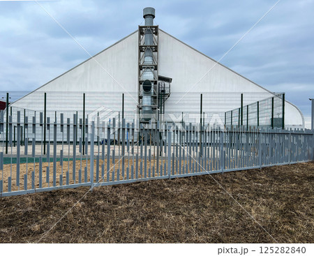 Industrial building with large ventilation system enclosed by a metal fence, set against a cloudy sky. Architecture showing functional and protective design elements 125282840