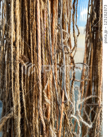 detailed view of natural fiber threads hanging close together, showcasing their varied textures and colors under sunlight. Highlights the organic and rustic appeal of raw fibers detailed view of natural fiber threads hanging close together, showcasing their varied textures and colors under sunlight. Highlights the organic and rustic appeal of raw fibers 125282873