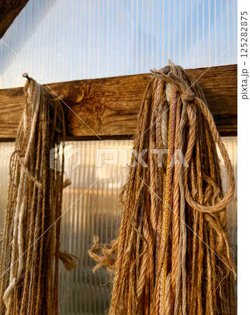 Natural fiber ropes in various textures and colors hang neatly from a wooden beam in a workshop setting, creating an artisanal and rustic atmosphere 125282875