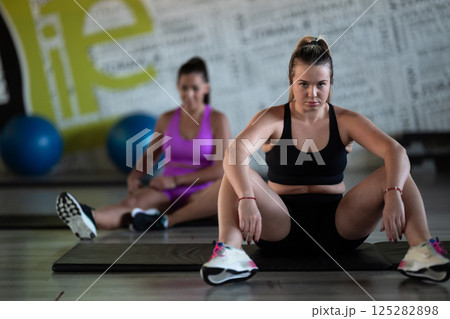 Two fitness women resting and recovering in the gym after an intense workout session, showcasing strength, endurance, and dedication to their fitness journey. 125282898