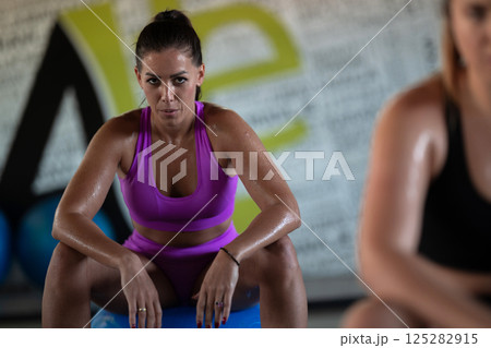 Two fitness women resting and recovering in the gym after an intense workout session, showcasing strength, endurance, and dedication to their fitness journey. 125282915