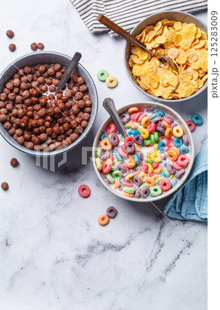Different types of breakfast cereals background. Chocolate balls, cornflakes and colorful fruit rings on white background. 125283009