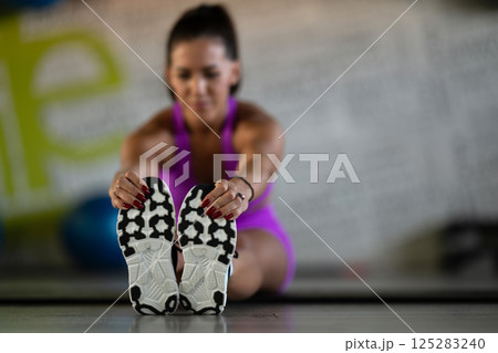 Woman Stretching in Gym. A athletic woman wearing a purple sports outfit is stretching her legs in a gym. 125283240