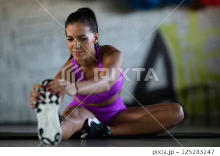 Woman Stretching in Gym. A athletic woman wearing a purple sports outfit is stretching her legs in a gym. 125283247
