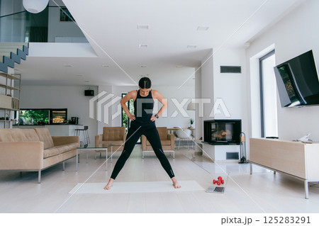 Young Beautiful Female Exercising, Stretching and Practising Yoga with Trainer via Video Call Conference in Bright Sunny House. Healthy Lifestyle, Wellbeing and Mindfulness Concept Young Beautiful Female Exercising, Stretching and Practising Yoga with Trainer via Video Call Conference in Bright Sunny House. Healthy Lifestyle, Wellbeing and Mindfulness Concept 125283291