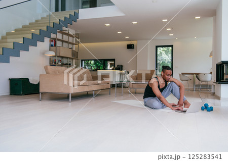 Training At Home. Sporty African American man doing the training while watching an online tutorial on a laptop, exercising in the living room, free space 125283541