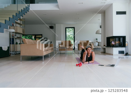 Young woman resting after online training while lying on the living room floor. 125283548