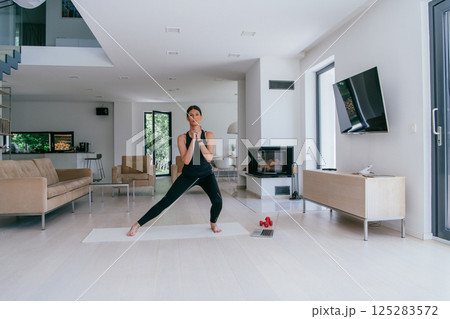 Young Beautiful Female Exercising, Stretching and Practising Yoga with Trainer via Video Call Conference in Bright Sunny House. Healthy Lifestyle, Wellbeing and Mindfulness Concept 125283572