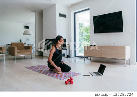 Young Beautiful Female Exercising, Stretching and Practising Yoga with Trainer via Video Call Conference in Bright Sunny House. Healthy Lifestyle, Wellbeing and Mindfulness Concept 125283724