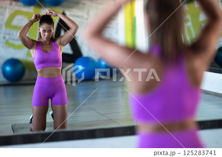 A determined woman ties her hair in preparation for an intense workout, embodying focus and strength as she gears up for her fitness training session A determined woman ties her hair in preparation for an intense workout, embodying focus and strength as she gears up for her fitness training session 125283741